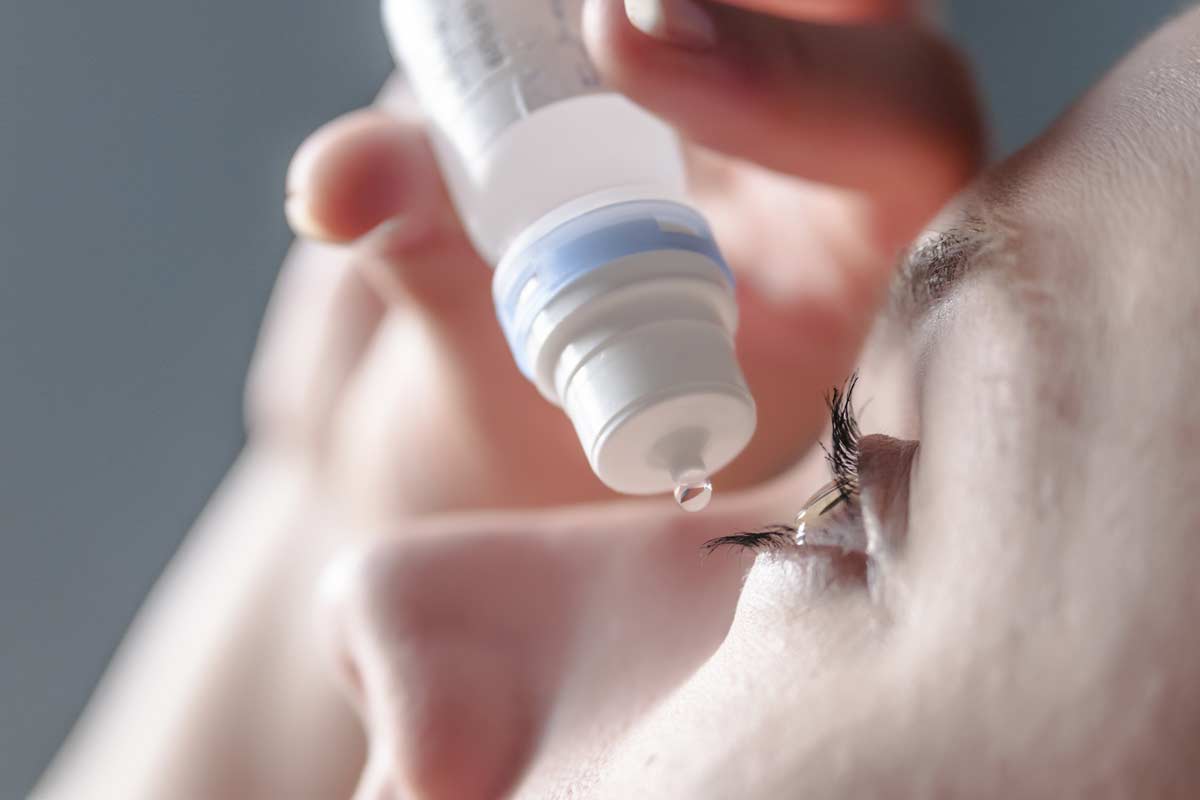 Close up view of young woman applying eye drop to left eye, arti